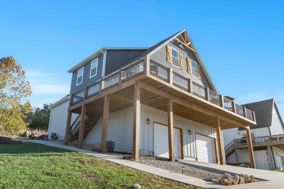 The elevated deck of the home is surrounded by greenery, with unique architectural features and outdoor furniture arranged for relaxation and gatherings. The lush surroundings hint at the home’s private, serene setting, perfect for starting or ending a day of Branson adventures.