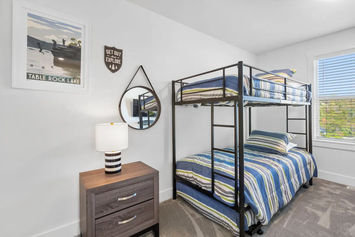 A cozy bunk room featuring a sturdy bunk bed, a nightstand with a lamp, playful wall art, and a decorative mirror. The arrangement feels adventurous and fun, ideal for children or young-at-heart guests.