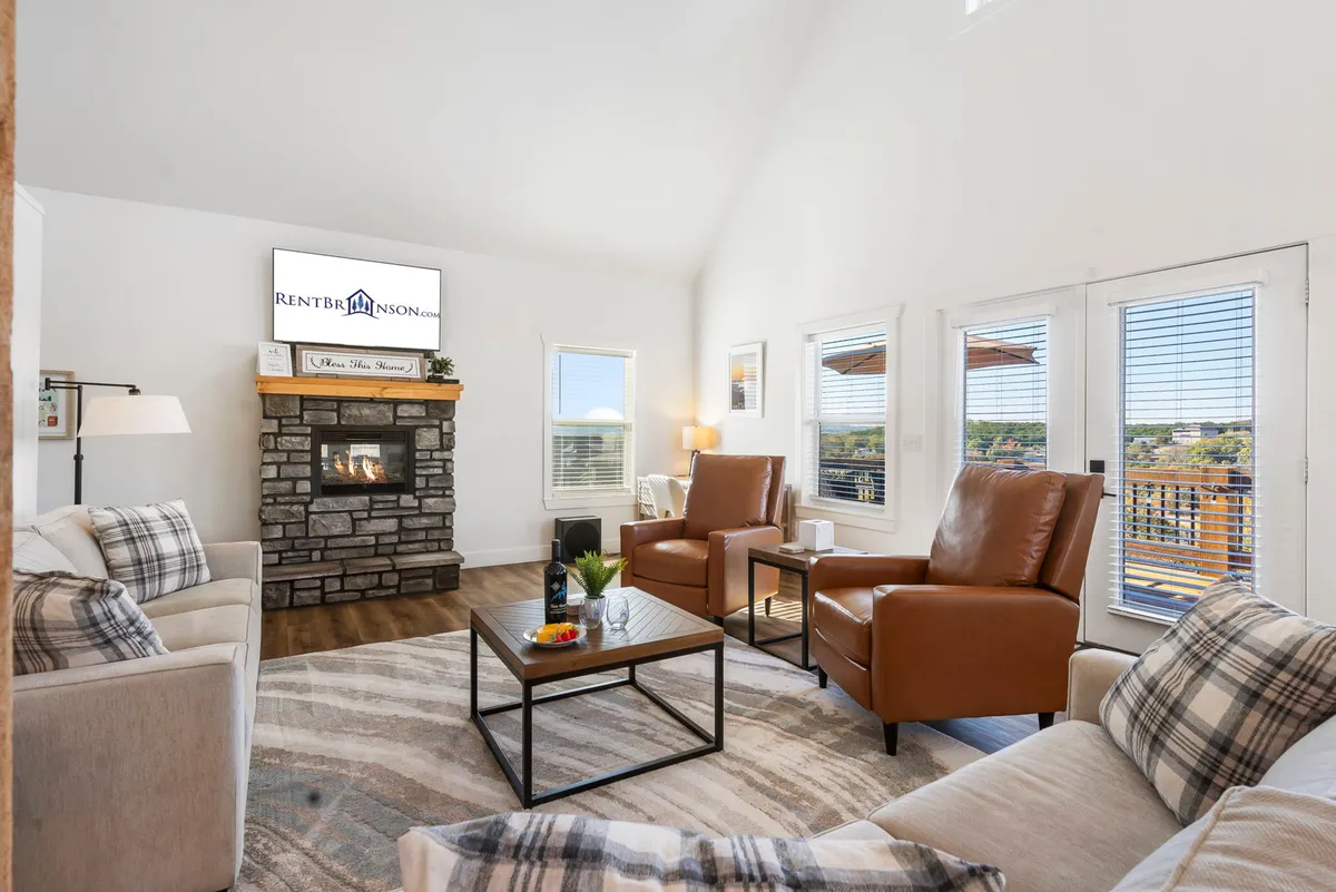 A cozy living room with a fireplace, large windows that flood the room with natural light, a TV, and comfortable armchairs. The decor is modern yet homey, with a coffee table inviting guests to unwind together after a day of adventure.
