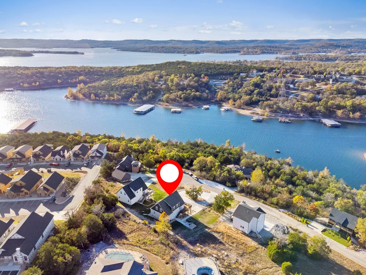 A sweeping exterior view capturing the lake, surrounding houses nestled among trees, and a winding road. The image radiates serenity, with the calm waters reflecting sunset colors and the natural landscape inviting outdoor activities.