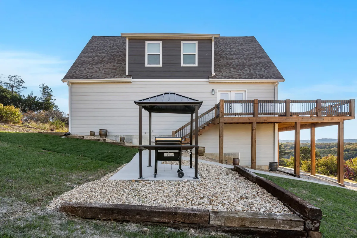 A close-up of the deck area featuring a grill, wooden decking, and the house’s exterior. The setup suggests easy access for outdoor cooking and is arranged for socializing and relaxation, with the lake view glimpsed beyond the railing.