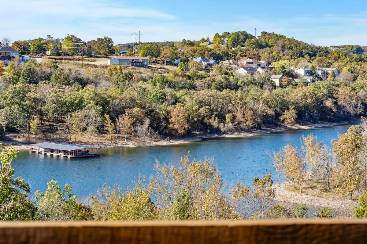 A tranquil view of Table Rock Lake, framed by trees along the shore and dotted with houses on the hillside. The calm water and scenic landscape capture the relaxed lakeside atmosphere, with hints of recreational activities such as fishing, boating, and hiking visible along the shoreline.